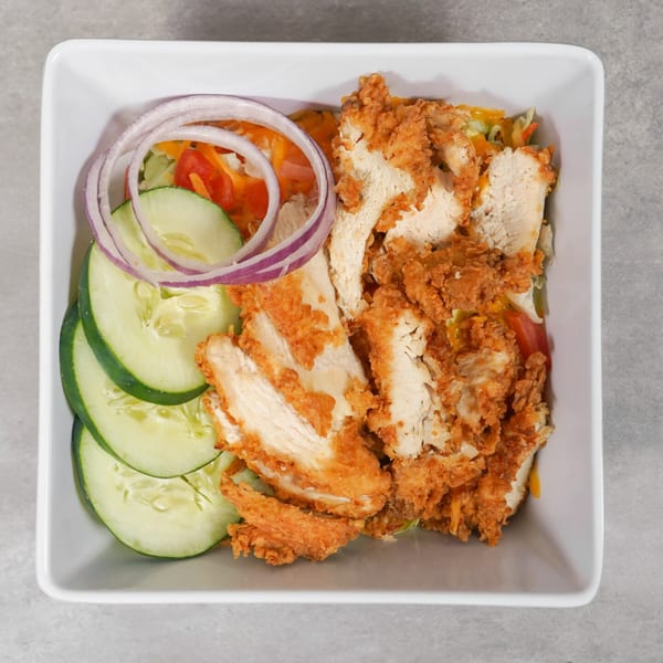 Crispy fried chicken strips, cucumber slices, red onion, and mixed greens in a white bowl.