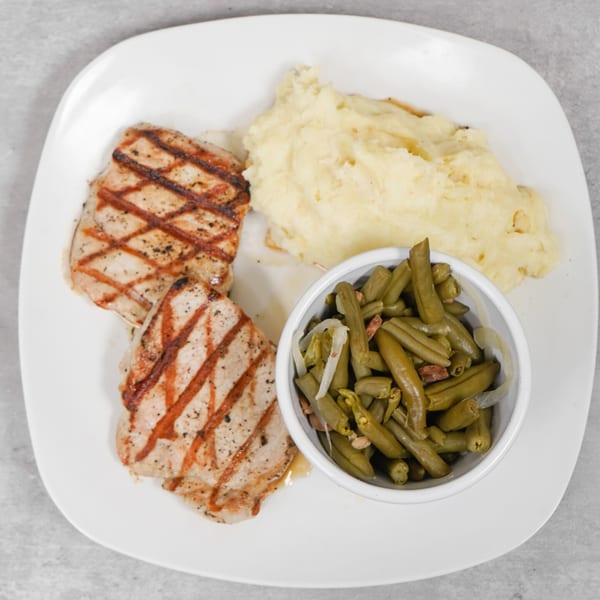 Grilled pork chops with mashed potatoes and a side of green beans with onions.