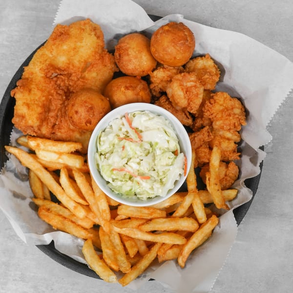 Fried fish, shrimp, hush puppies, french fries, and coleslaw served in a black basket.