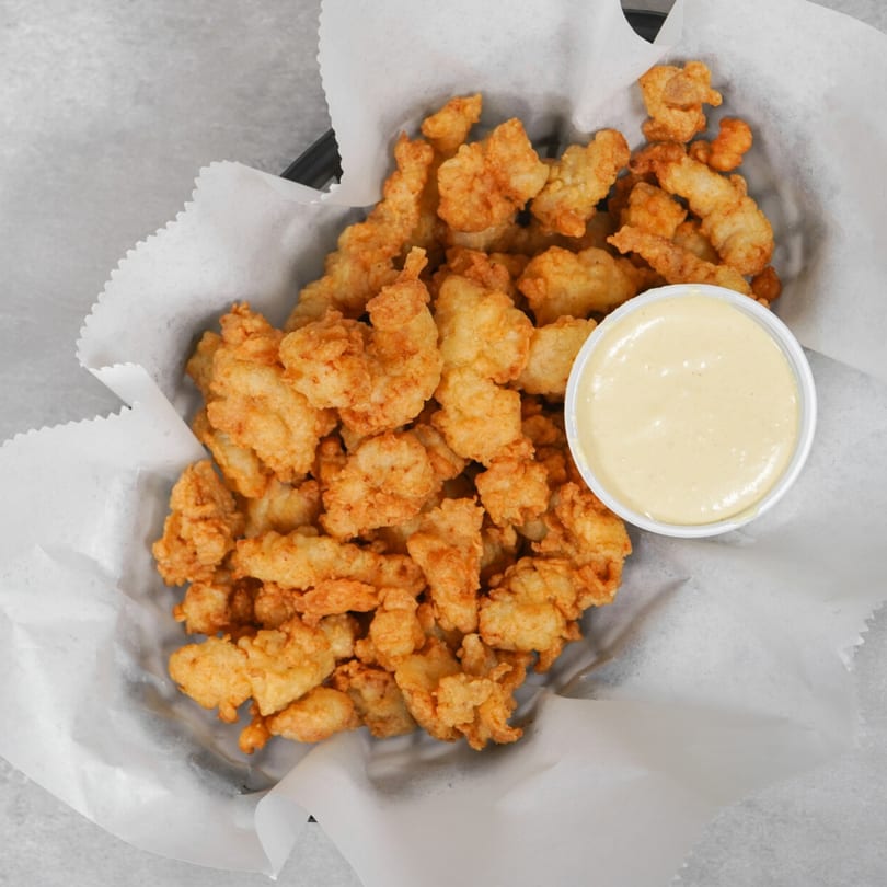 Crispy fried clam strips in a basket lined with white paper, served with a side of dipping sauce.