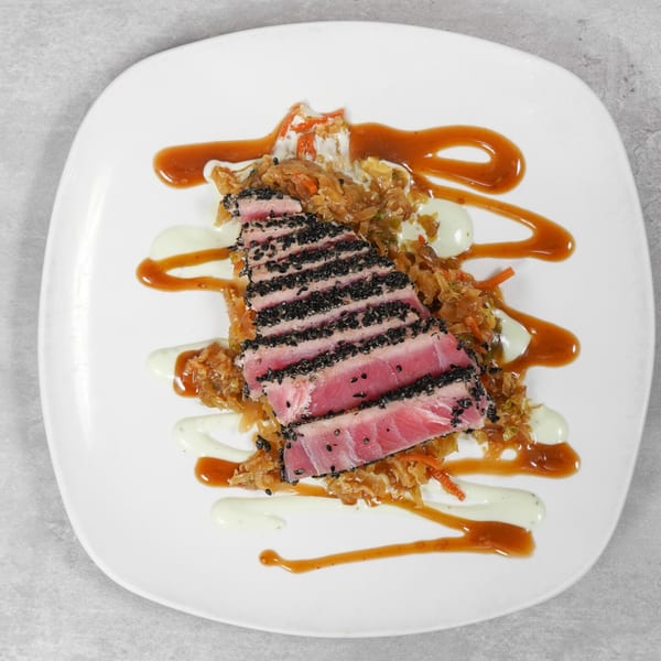 Seared tuna with black sesame crust, served over sautéed cabbage with two sauces.