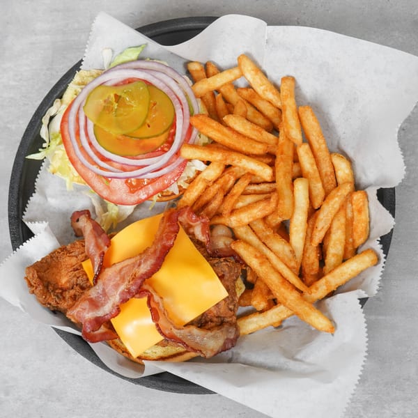 Top-down view of a fried chicken sandwich with bacon, cheese, and fries in a basket with fries.