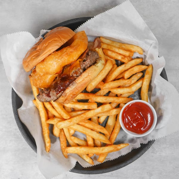 A cheesesteak sandwich with fries and a side of ketchup in a black basket.