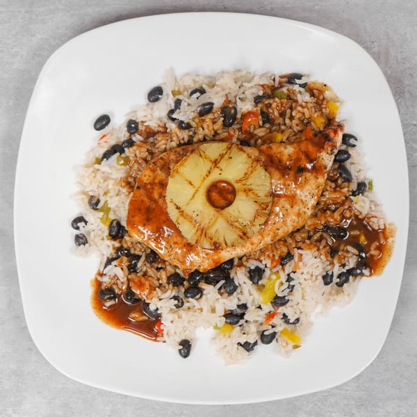 Grilled chicken breast with pineapple, rice, and black beans on a white plate.