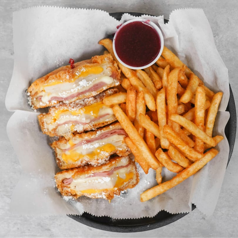 Deep-fried ham and cheese sandwiches with powdered sugar, fries, and a side of berry sauce.