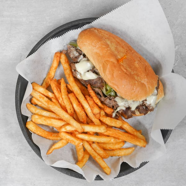 A cheesesteak sandwich with peppers and onions, served with a side of golden french fries.